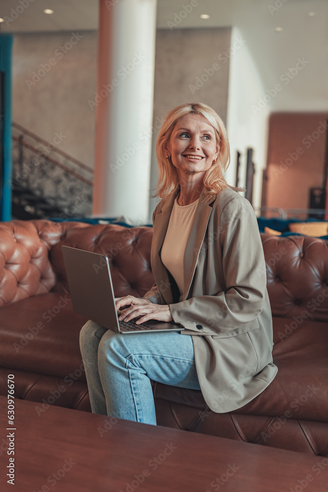 Smiling woman sales manager sitting on sofa and working on laptop on coworking background Smiling woman sales manager sitting on sofa and working on laptop on coworking background