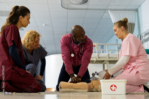 Senior african american male doctor with diverse trainee doctors learning cpr on model at hospital photo