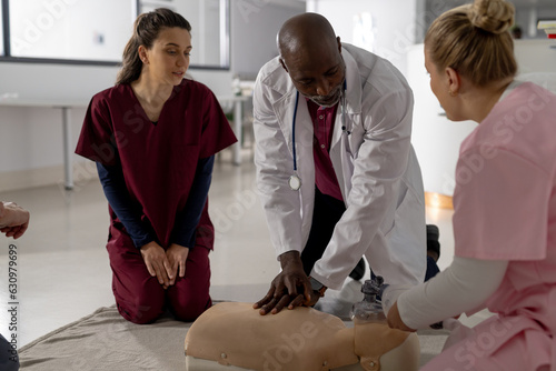 Senior african american male doctor with diverse trainee doctors learning cpr on model at hospital