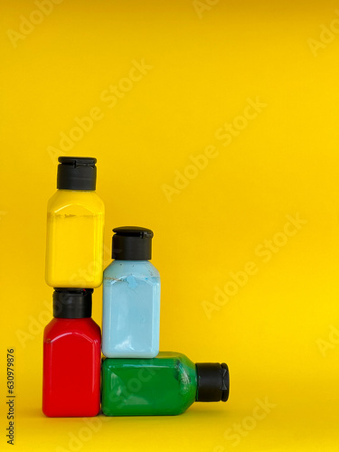 Bottles with bright multi-colored acrylic paint on a yellow background