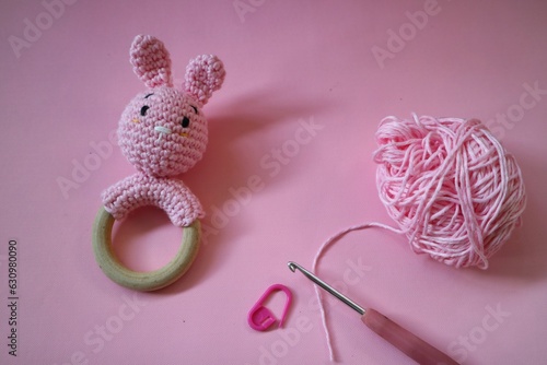 Crocheted Pink Bunny rattle with cotton yarn and neele hook isolated on pink background. Craft concept. Baby toy handmade. Pink knitted rabbit for children. Handmade rattle toy for newborn baby. photo