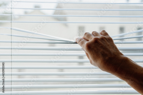 The woman opens and closes the horizontal white blinds with her hands.