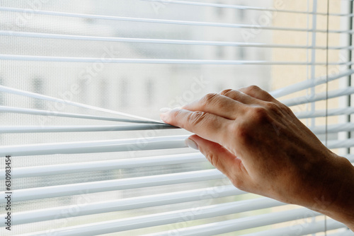 The woman opens and closes the horizontal white blinds with her hands.