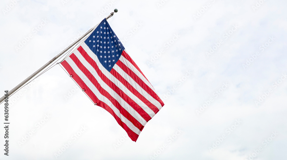 United States of America flag on a pole waving on cloudy sky background.