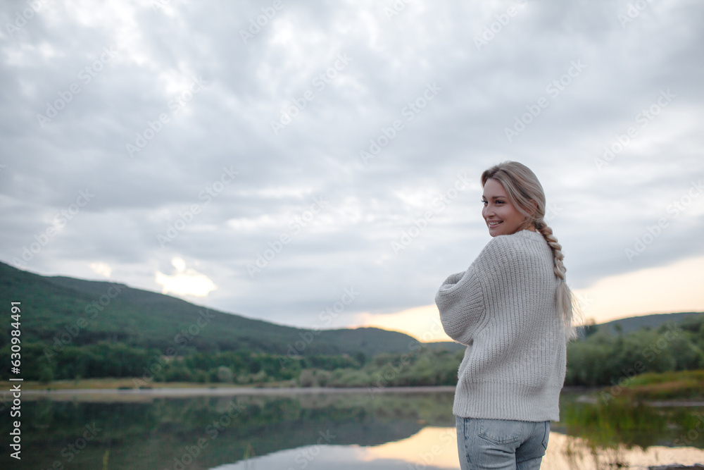 Back view of the blond woman dressed sweater and jeans., Walking in the shore of the lake with beautiful landskape. The girl enjoy the nature in her trip Back view of the blond woman dressed sweater and jeans., Walking in the shore of the lake with beautiful landskape. The girl enjoy the nature in her trip