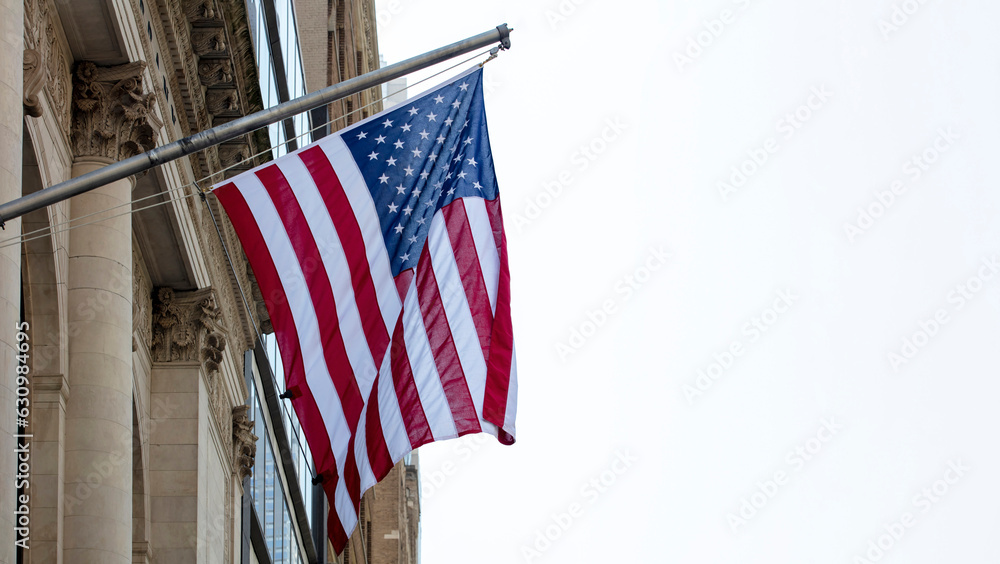 United States of America flag on a building facade waving on cloudy sky background