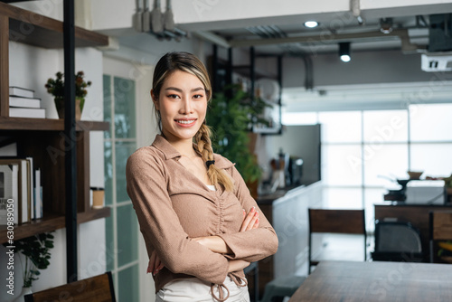Young asian business woman standing post near desk in home office. Beautiful business female in suit working at home holding pen. Attractive woman smiling looking at camera.