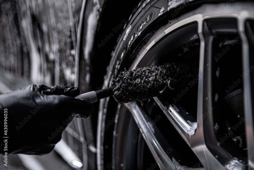 Employee of a car wash or car detailing studio cleans the aluminum rims of a modern car