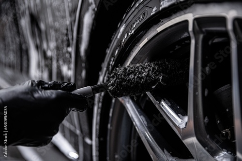 Employee of a car wash or car detailing studio cleans the aluminum rims of a modern car photo