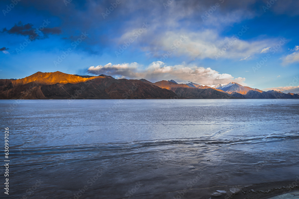 Pangong Lake during the blue hour, where fully frozen waters reflect the majestic mountain peaks in the distance, creating a scene of pure winter enchantment