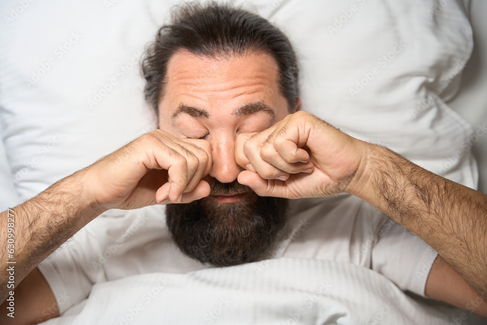Bearded male wakes up on a snow-white bed Bearded male wakes up on a snow-white bed