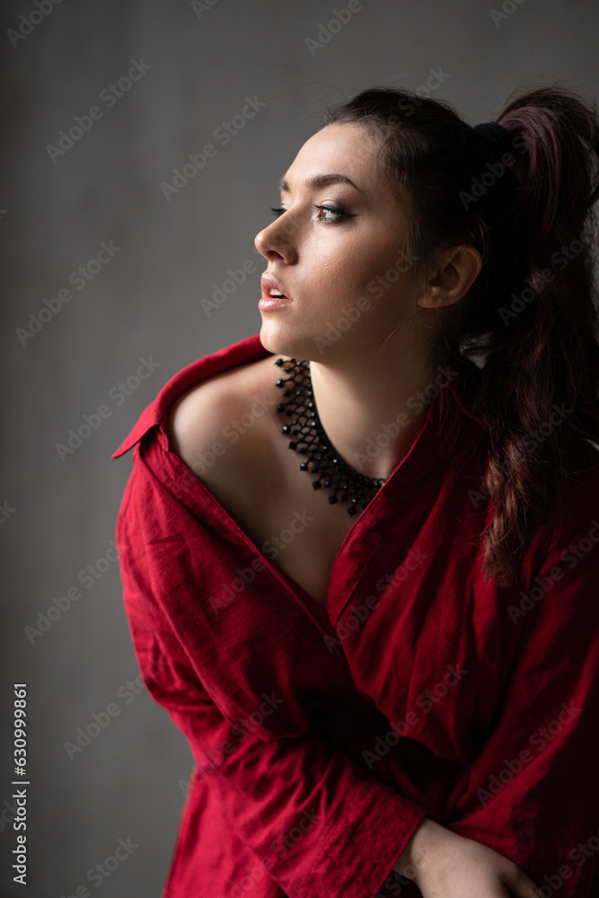 a beautiful young girl in a red shirt with a necklace with a handmade ornament on her neck is posing in a photo studio a beautiful young girl in a red shirt with a necklace with a handmade ornament on her neck is posing in a photo studio