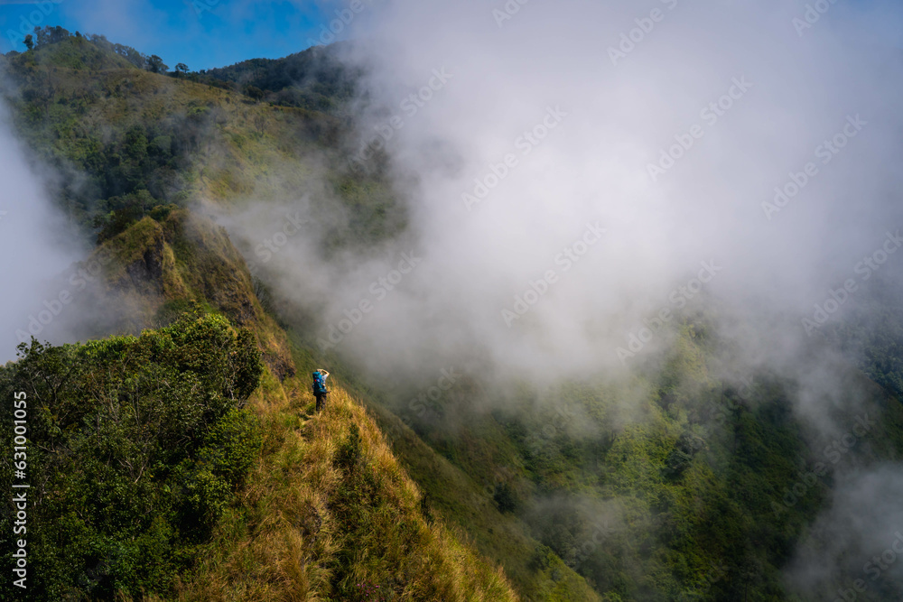 a person with blue backpack and camera standing in the middle of mountain range and sea of cloud in northern of thailand (Nan province, Thailand) เด่นช้างนอน