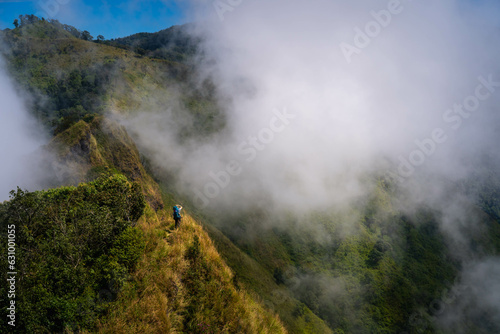 a person with blue backpack and camera standing in the middle of mountain range and sea of cloud in northern of thailand (Nan province, Thailand) เด่นช้างนอน