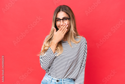 Young Uruguayan woman isolated on red background happy and smiling covering mouth with hand
