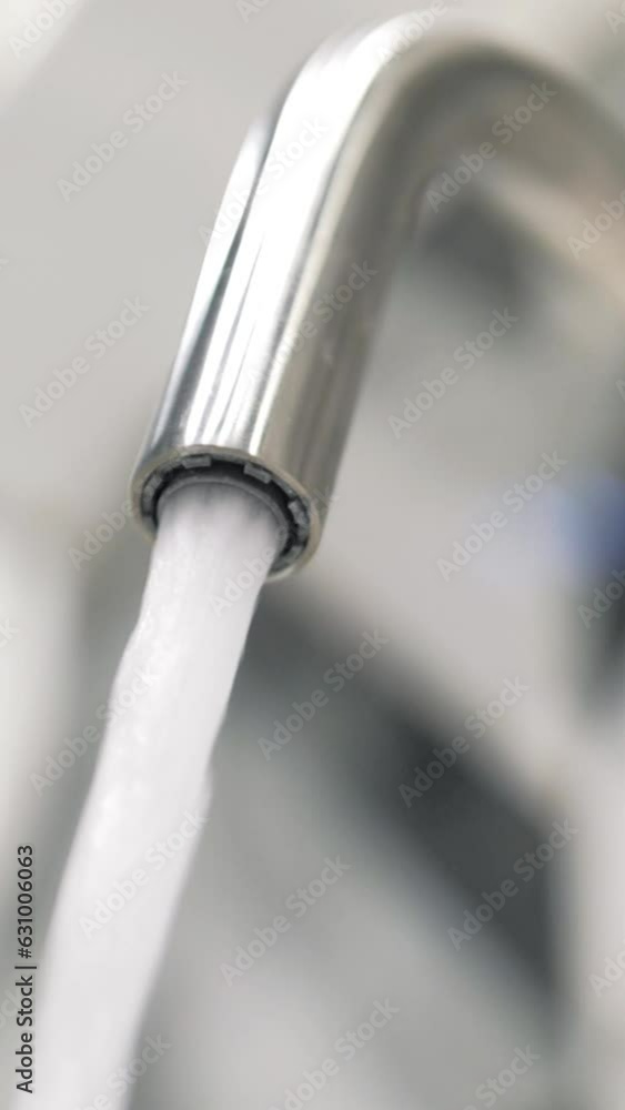 vertical video water pouring from a faucet tap slow motion. The strong water pressure flowing from a stylish chrome tap indoors vertical video water pouring from a faucet tap slow motion. The strong water pressure flowing from a stylish chrome tap indoors