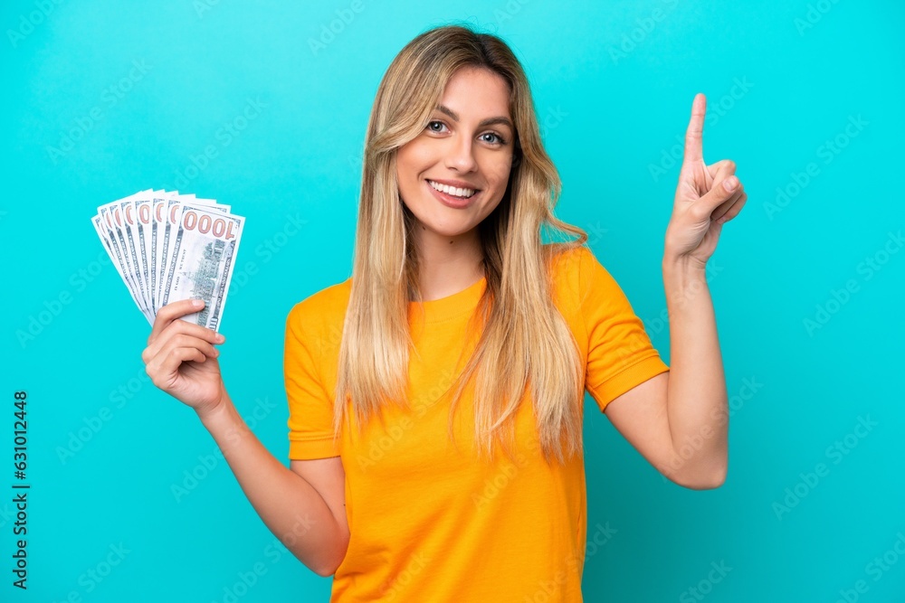 Young Uruguayan woman taking a lot of money isolated on blue background pointing up a great idea Young Uruguayan woman taking a lot of money isolated on blue background pointing up a great idea