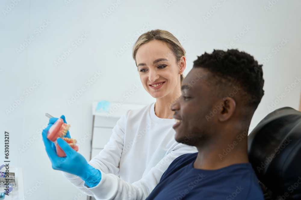 Fototapeta premium Dental technician showing dental prosthesis to African American client