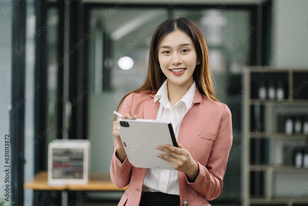 Asian woman holding tablet working at desk, standing smiling looking at camera. Asian woman holding tablet working at desk, standing smiling looking at camera.