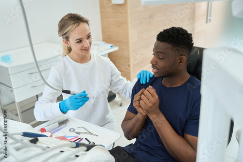 Принти на полотні Dentist taking dental drill and assuring patient that it will not hurt