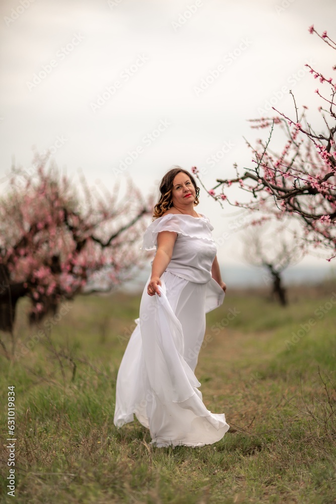 Woman peach blossom. Happy woman in white dress walking in the garden of blossoming peach trees in spring Woman peach blossom. Happy woman in white dress walking in the garden of blossoming peach trees in spring