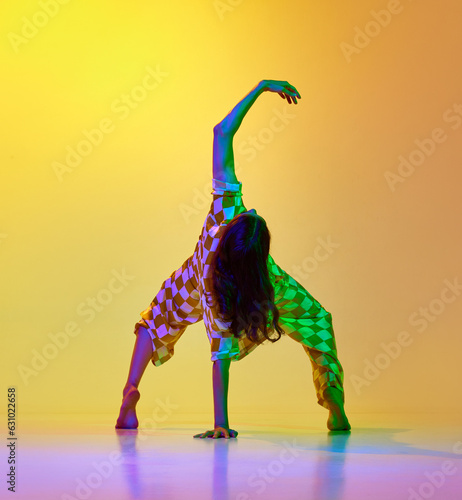 Dynamic image of flexible, artistic young woman dancing against gradient yellow orange background in neon light. Concept of modern dance style, hobby, art, performance, lifestyle, ad photo