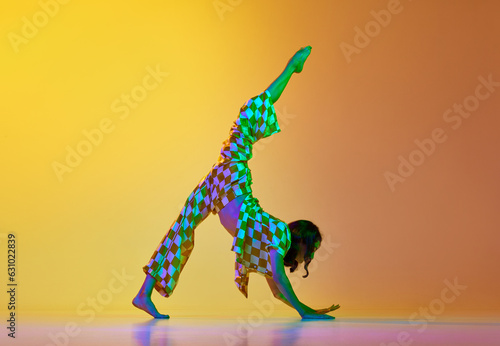 Twine pose. Young talented woman, professional dancer in motion, dancing against gradient yellow orange background in neon light. Concept of modern dance style, hobby, art, performance, lifestyle, ad photo