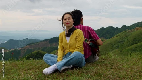 A couple sitting back to back in the mountains, Man playing guitar sitting on the grass surrounded by mountains, Slow motion
