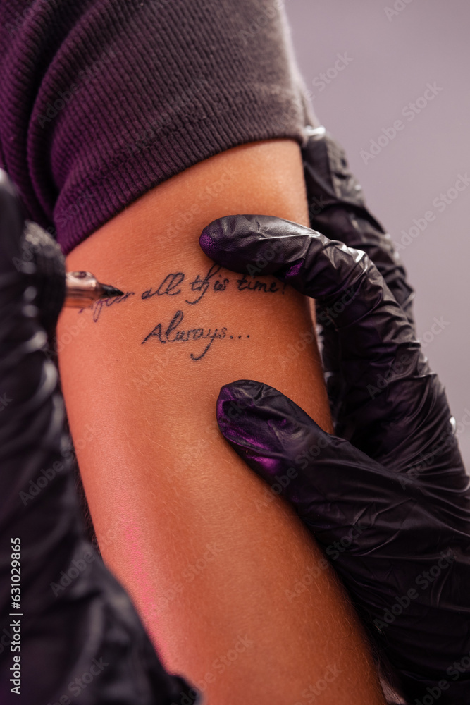 Hands of professional tattoo artist creating inscriptions on arm of woman