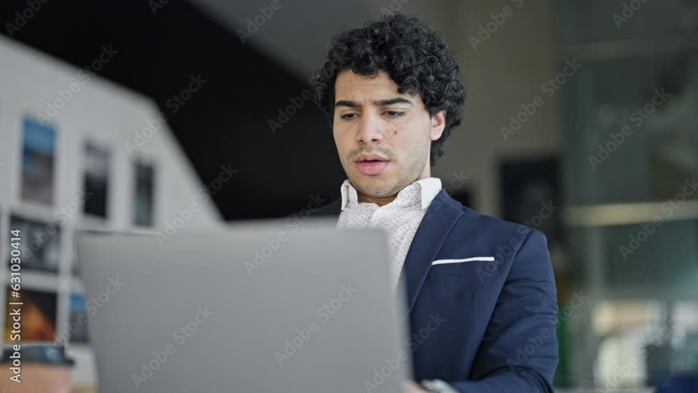 Young latin man business worker using laptop looking upset at office Young latin man business worker using laptop looking upset at office