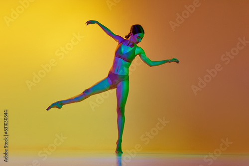Full-length image of young woman, professional dancer in motion, dancing in underwear against gradient yellow orange background in neon light. Concept of modern dance style, hobby, art, lifestyle, ad