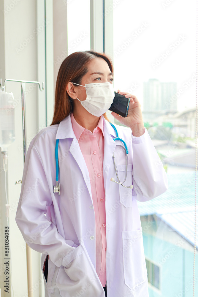 Asian female doctor wearing a surgical mask standing and talking on the phone. medical concept Asian female doctor wearing a surgical mask standing and talking on the phone. medical concept