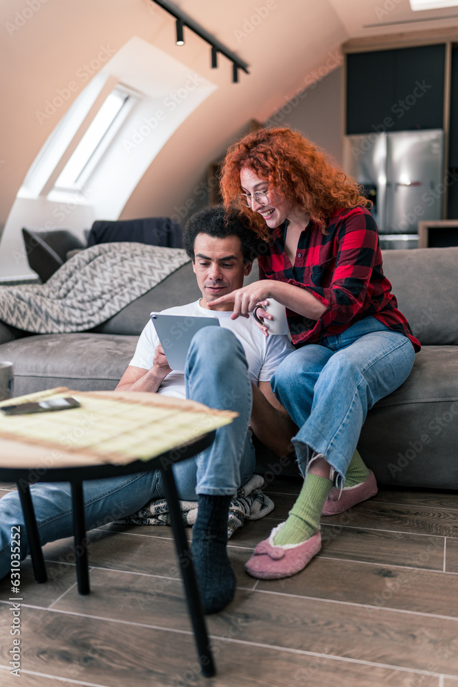 An interracial couple is sitting in the living room looking for restaurants to celebrate their anniversary using a tablet An interracial couple is sitting in the living room looking for restaurants to celebrate their anniversary using a tablet