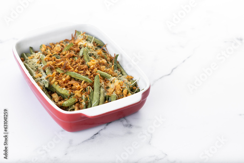 A traditional green bean casserole topped with French Fried Onions and cream of mushroom on white marble. Copy space