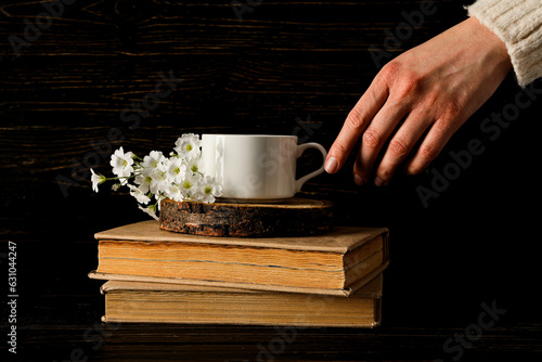 Cup on wooden stand and books, female hand on wooden background