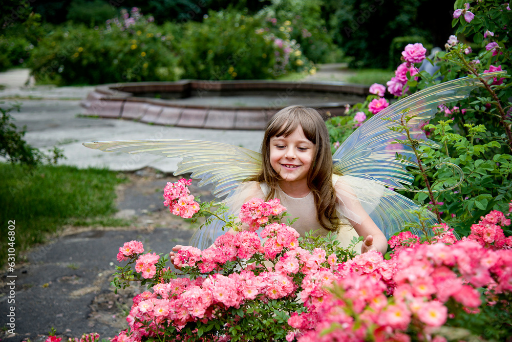 Naklejka premium little beautiful girl in a fairy costume of butterfly with wings in princess dress having fun in roses garden on sunny summer day 