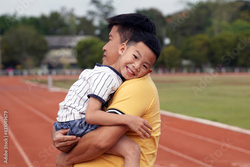 father holding his son on his shoulder boy smiling happily While going for a walk at the nearby stadium in the evening. Outdoor activities concept with family, father and son. 
