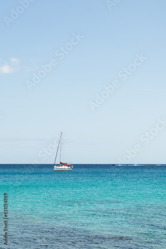 Seascape. Turquoise blue sea with sailboat in the background, sky with white clouds. Fuerteventura, Canary Islands, Spain 