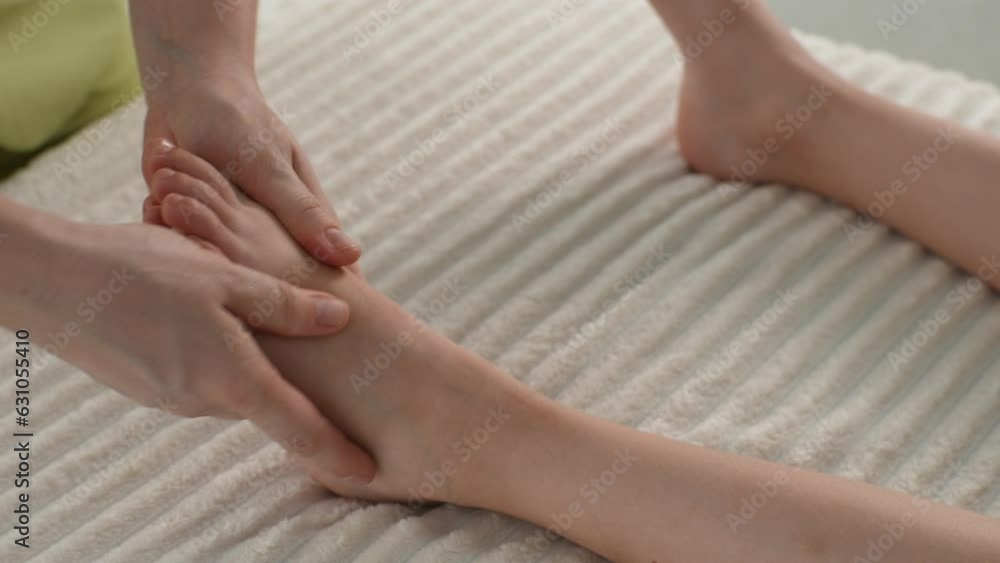 Close-up hands of unrecognizable female masseur doing orthopedic leg exercises of teenager girl client, kneading her ankle, prevention of pain in heel. Concept of healthy childcare, slow motion. Close-up hands of unrecognizable female masseur doing orthopedic leg exercises of teenager girl client, kneading her ankle, prevention of pain in heel. Concept of healthy childcare, slow motion.