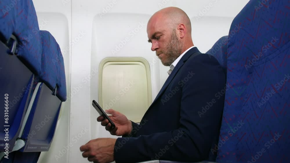 A man with a beard and bald head using cell phone smartphone on an airplane airliner sitting in the passenger cabin A man with a beard and bald head using cell phone smartphone on an airplane airliner sitting in the passenger cabin