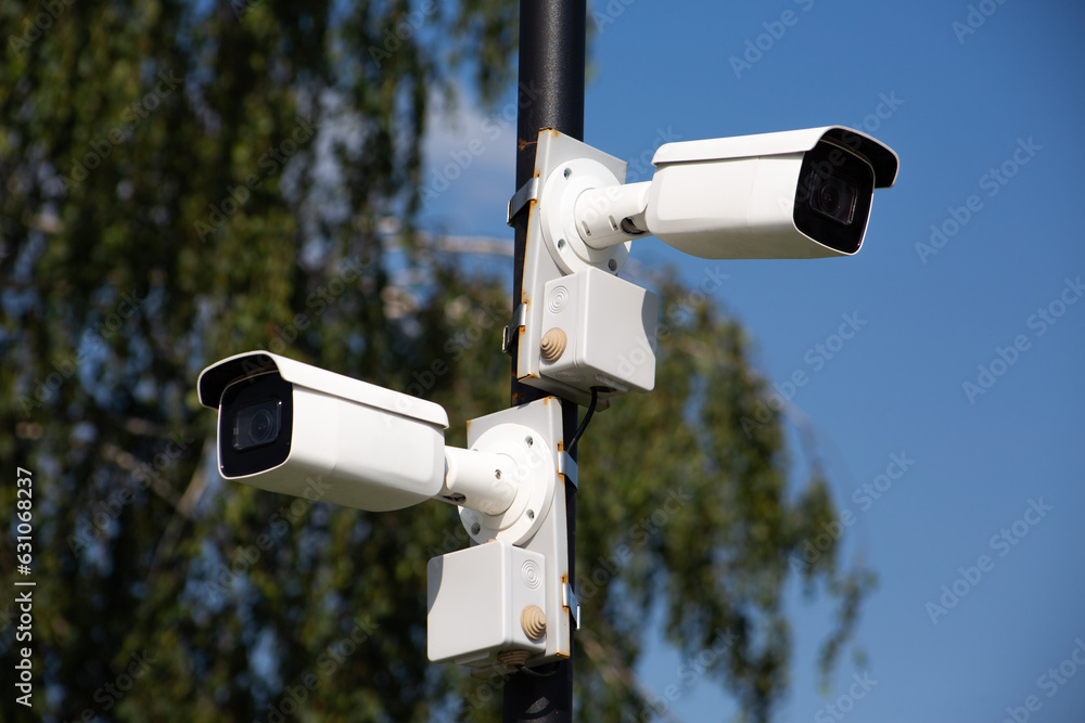 Two white surveillance cameras on a pole look in different directions for security on a city street