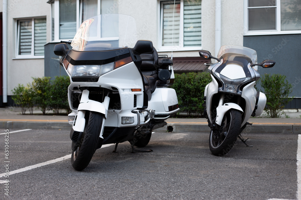 Two white motorcycles are parked in the same parking space near an apartment building