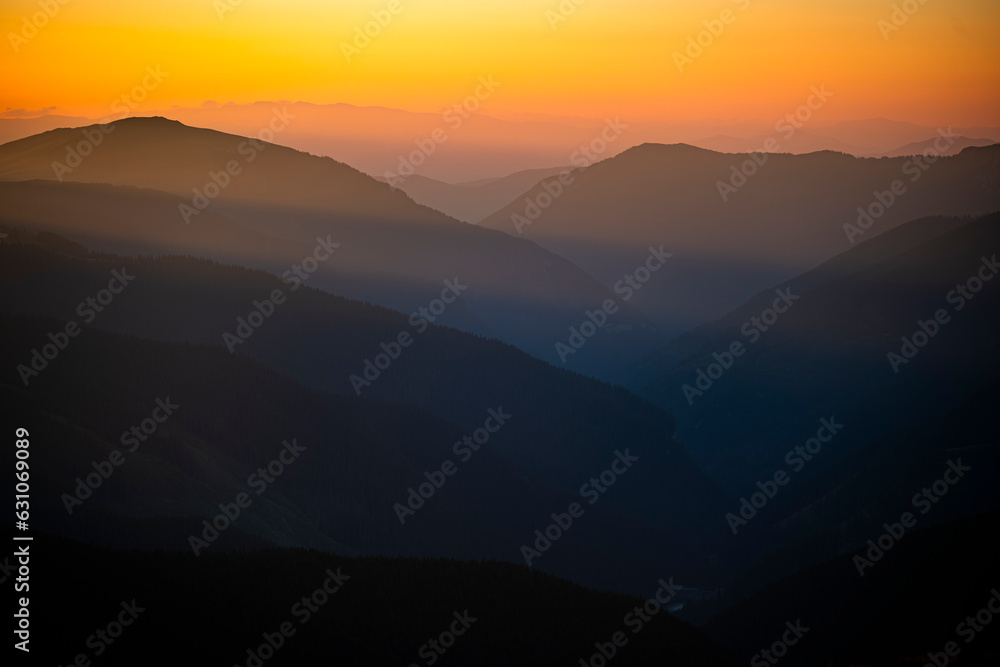 Dark silhouettes of mountains at sunrise with an orange sky. Dark background with a copy space. The Parang Mountains, Romania.