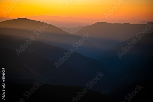 Dark silhouettes of mountains at sunrise with an orange sky. Dark background with a copy space. The Parang Mountains, Romania.