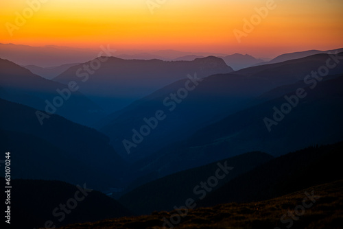 Dark silhouettes of mountains at sunrise with an orange sky. Dark background with a copy space. The Parang Mountains, Romania.