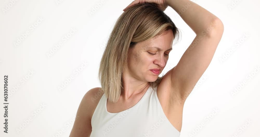Female in white shirt stands and sniffs armpits at white studio wall. Woman tingling from unpleasant body odor. Unpleasant sweat odor slow motion Female in white shirt stands and sniffs armpits at white studio wall. Woman tingling from unpleasant body odor. Unpleasant sweat odor slow motion