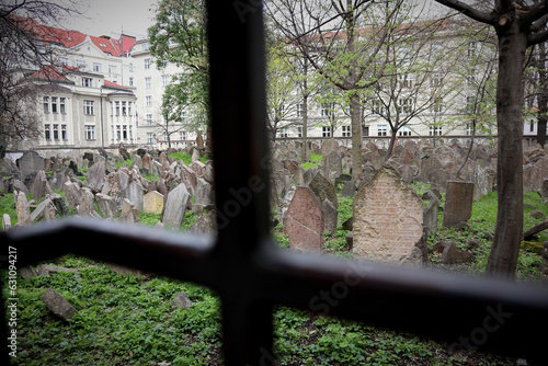 Very old and weathered Jewish gravestones in a walled-in cemetery in Prague photographed through a small iron-barred peephole