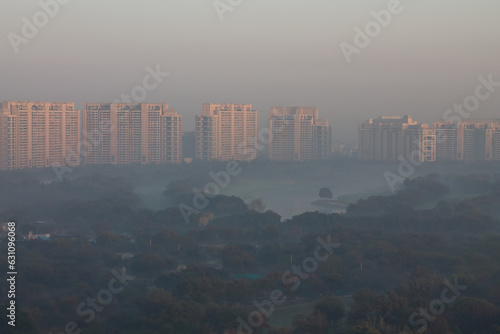 Sunrise in Gurgaon urban skyline with luxury residential apartments.Winter morning fog on the lake,golf course and rising above water to create the magic.Modern architecture of Gurugram cityscape.