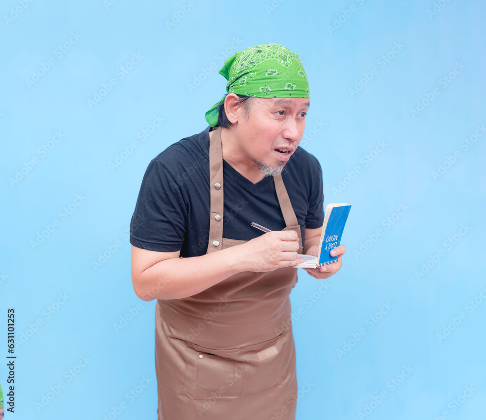 An attentive middle-aged barista taking orders and writing it in his notebook. Isolated on a blue background.