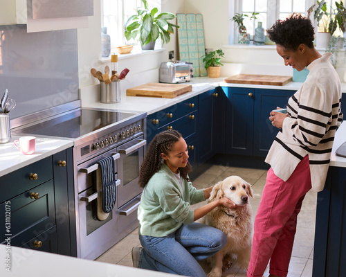 Mother Talking With Teenage Daughter Relaxing At Home In Kitchen With Pet Dog